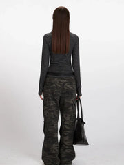 Back view of a model wearing a gray striped long-sleeve top with a mock neck and thumbholes, paired with camouflage cargo pants and a black belt, holding a black tote bag.