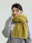 Model wearing a chunky knit scarf in a lime green hue, tied around the neck, over a grey sweater.