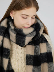 Close-up of a woman wearing a cream cable knit sweater and a large black and beige plaid scarf with fringe around her neck.