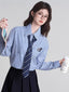 Model wearing a light blue striped button-down shirt with a navy striped tie and a black pleated skirt, holding a pink wallet and a coffee cup.
