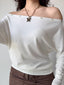 Woman wearing a white off-the-shoulder knit top with decorative buttons and a butterfly necklace.