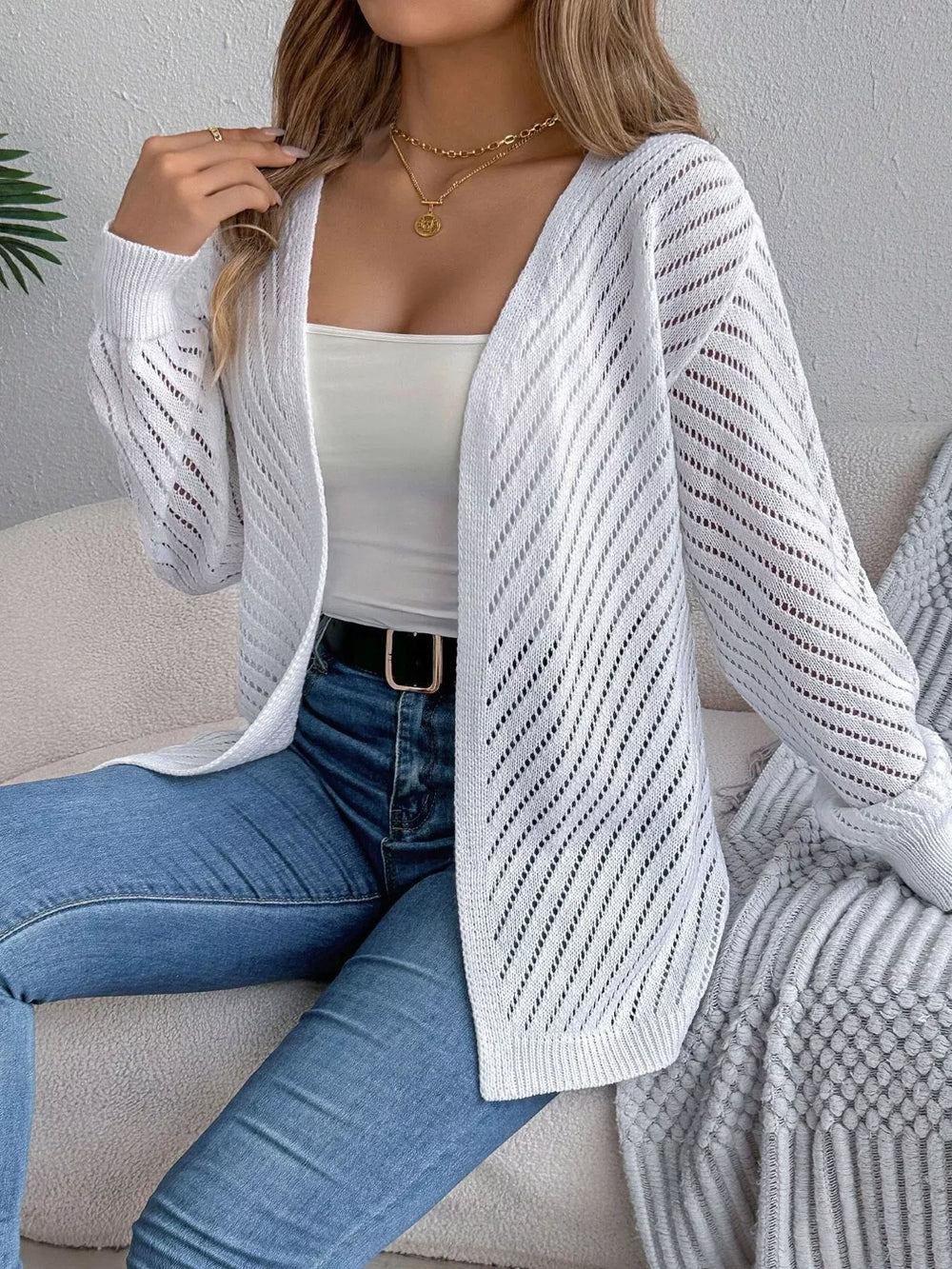 Woman wearing a white open-front knit cardigan over a white tank top and blue jeans.