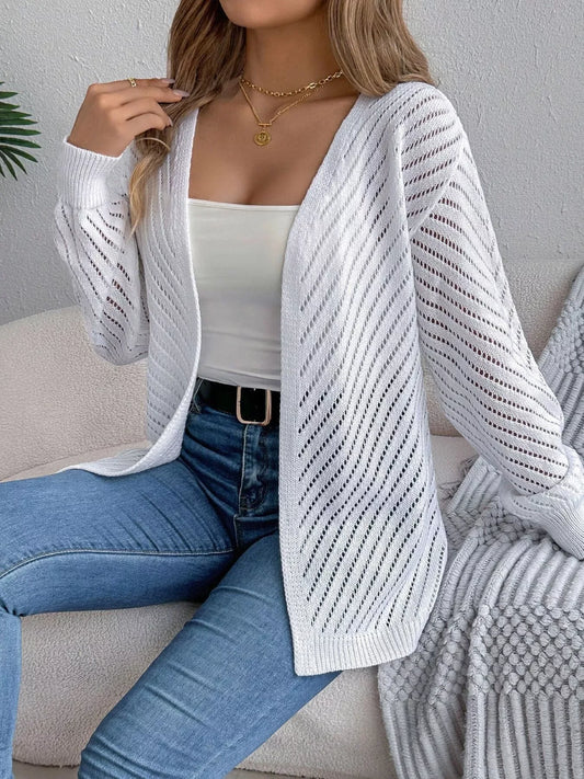 Woman wearing a white open-front knit cardigan over a white tank top and blue jeans.