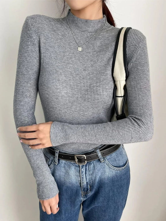 Woman wearing a gray ribbed mock neck long sleeve sweater with blue jeans and a black belt
