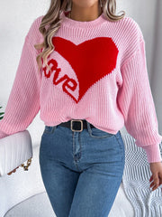 Woman wearing a pink knit sweater with a red heart graphic and the word "love" on the front, holding a white handbag.