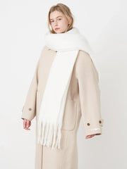 Woman wearing a white fluffy scarf draped over a beige coat, angled front view