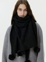 Close-up of a woman wearing a black knit scarf with pom-pom embellishments