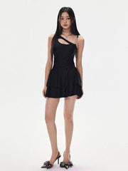 Woman in a black asymmetrical cutout dress with a tiered skirt and high heels, standing and looking forward.