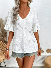 A woman stands wearing a white eyelet top with ruffled short sleeves and denim shorts.