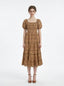 Woman wearing a brown puff-sleeve midi dress with a smocked bodice and tiered skirt featuring a sun and geometric print, standing against a white background.