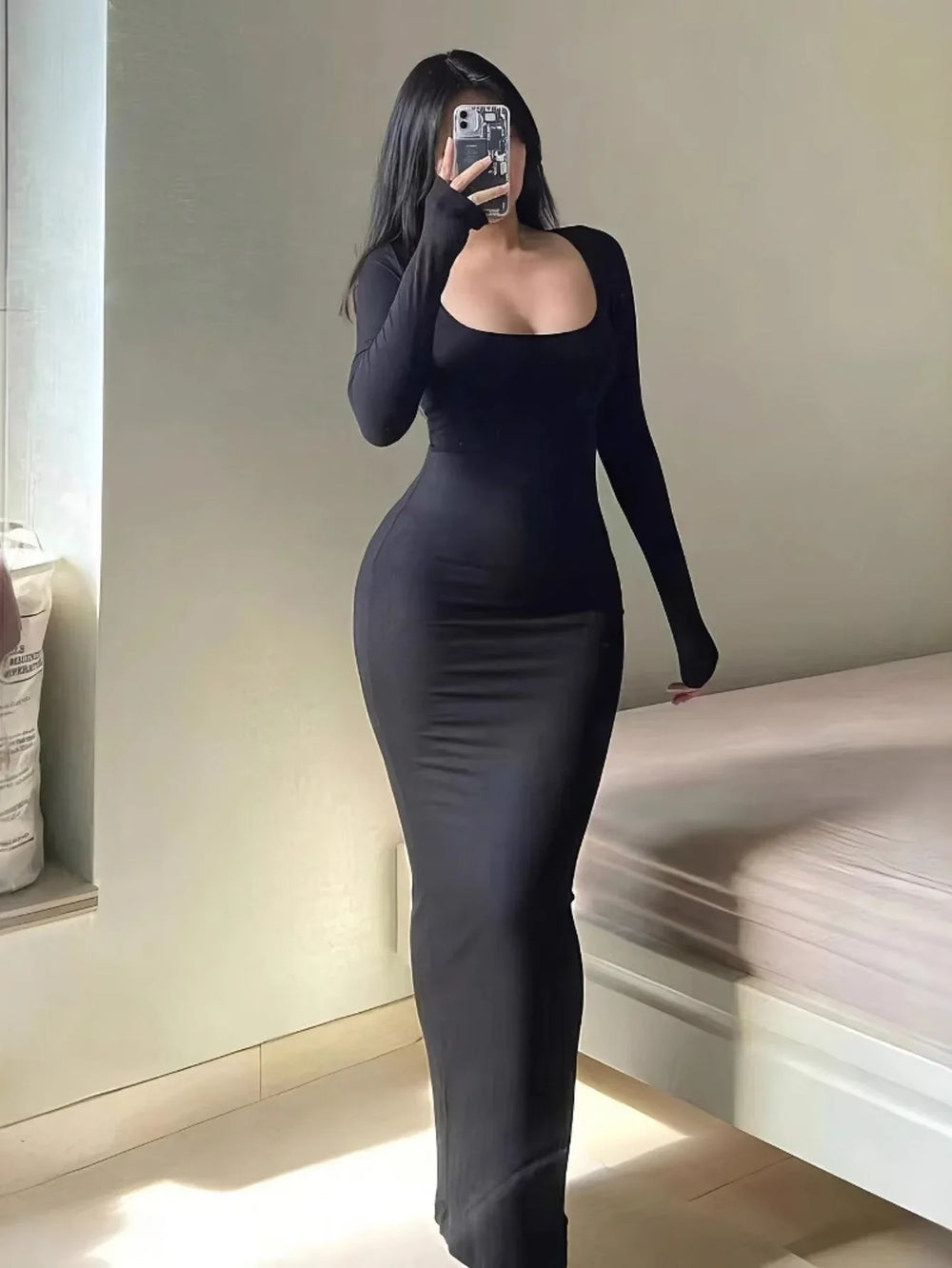 Woman wearing a long-sleeved, scoop-neck, form-fitting, floor-length mermaid silhouette dress in black, posing in a room.