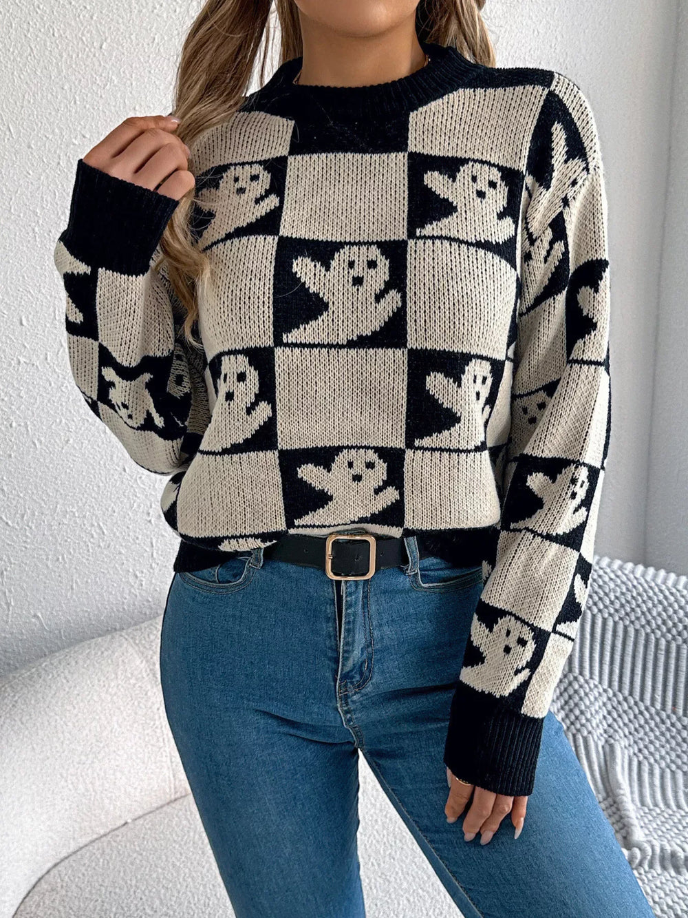 Front view of a woman wearing a black and white ghost print checkerboard knit sweater with blue jeans and a black belt.