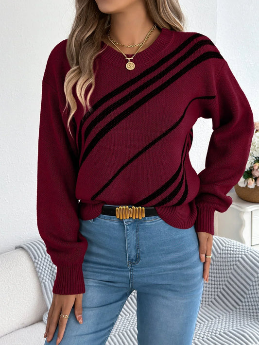 Woman wearing a burgundy knit sweater with black diagonal stripes, blue jeans, and a gold necklace.