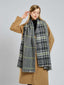 Woman in a tan coat adjusting her large houndstooth and plaid scarf