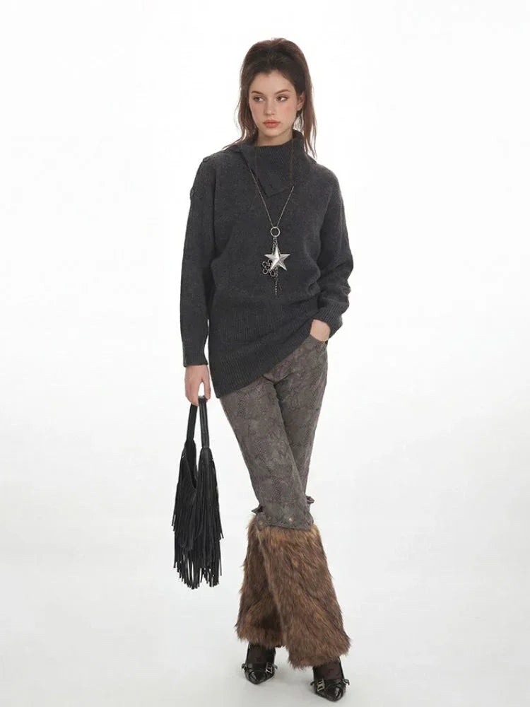 Woman in a charcoal grey oversized turtleneck knit tunic, patterned leggings, and brown furry leg warmers, holding a black fringed handbag.