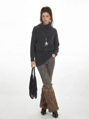 Woman in a charcoal grey oversized turtleneck knit tunic, patterned leggings, and brown furry leg warmers, holding a black fringed handbag.