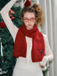 Woman wearing a red knit scarf with embroidered bow detail and text, standing next to a Christmas tree.
