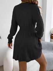 Rear view of a woman wearing a black long-sleeved knit dress with cable knit detailing on the bodice and an A-line skirt.