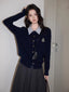 Woman wearing a navy blue cable knit cardigan with a striped collar and a gray pleated skirt.