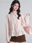 Woman wearing a light pink ruffled peplum blouse with a Peter Pan collar and lace trim, holding a pink handbag.
