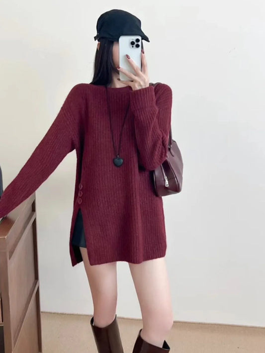 Woman wearing a burgundy ribbed knit longline tunic with side slits and buttons, black shorts, and brown boots, holding a phone to take a mirror selfie.