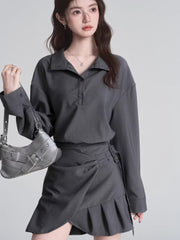 Model holding a silver handbag and wearing a grey long-sleeved collared shirt and a grey skirt.