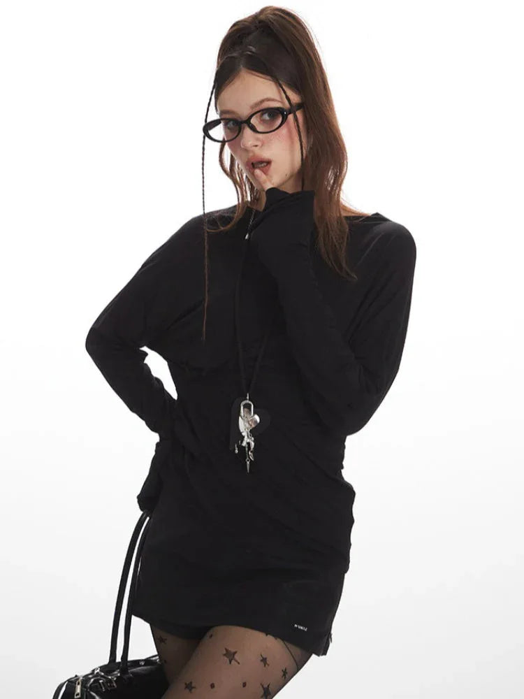 Woman wearing a black long-sleeve mini dress, star-patterned tights, and glasses, striking a pose.