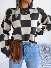 Woman wearing a black and white checkerboard knit sweater with light wash jeans and a brown fringe clutch, front view, showing more of the sweater.