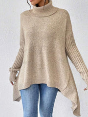 Front view of a woman wearing a beige oversized turtleneck sweater with an asymmetrical hem and ribbed sleeves.