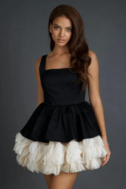 Model wearing a black and white short dress with a square neckline and a ruffled hem.