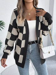 Woman wearing a black and cream checkerboard knit cardigan over a white tank top and blue jeans, holding a white quilted handbag.