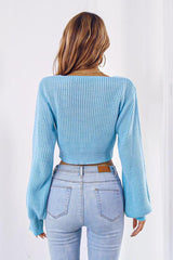Back view of a woman wearing a light blue cropped tie-front sweater with long puffed sleeves and light wash jeans