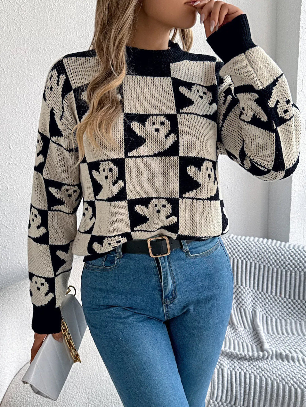 Close-up front view of a woman wearing a black and white ghost print checkerboard knit sweater with blue jeans.