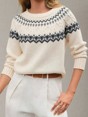 Woman wearing a cream-colored knit sweater with a Fair Isle pattern around the yoke and white trousers with a brown belt.