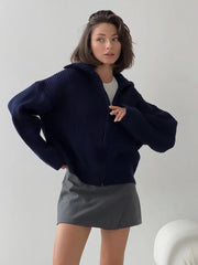 Woman wearing a navy blue zip-up cardigan over a white top and gray mini skirt.
