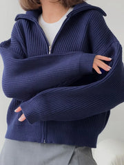 Close-up of the ribbed knit texture and oversized sleeves of a navy blue zip-up cardigan.