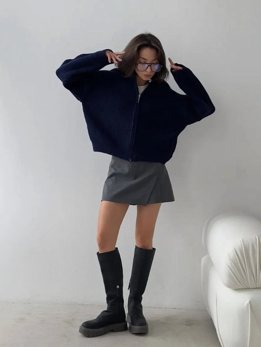 Woman wearing a navy blue oversized zip-up cardigan with a gray mini skirt and black boots.