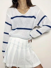 Woman wearing a white and blue striped v-neck sweater and a white pleated skirt, posing with hand on hip.