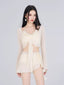 Woman wearing a cream-colored bikini set with a sheer long-sleeved cover-up tied at the front, paired with ruffled hem shorts.
