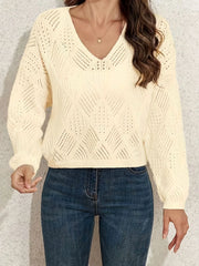Front view of a woman wearing a cream-colored V-neck cropped knit sweater with long sleeves and a diamond pattern, paired with blue jeans.