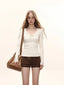 Model wearing a cream long-sleeve top with lace trim and a bow detail, paired with brown shorts and a brown shoulder bag.