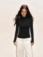 Woman wearing a black long-sleeve turtleneck top and white cargo pants, looking at the camera.