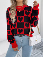 Woman wearing a red and black checkerboard heart print knitted sweater with light blue jeans and a white handbag