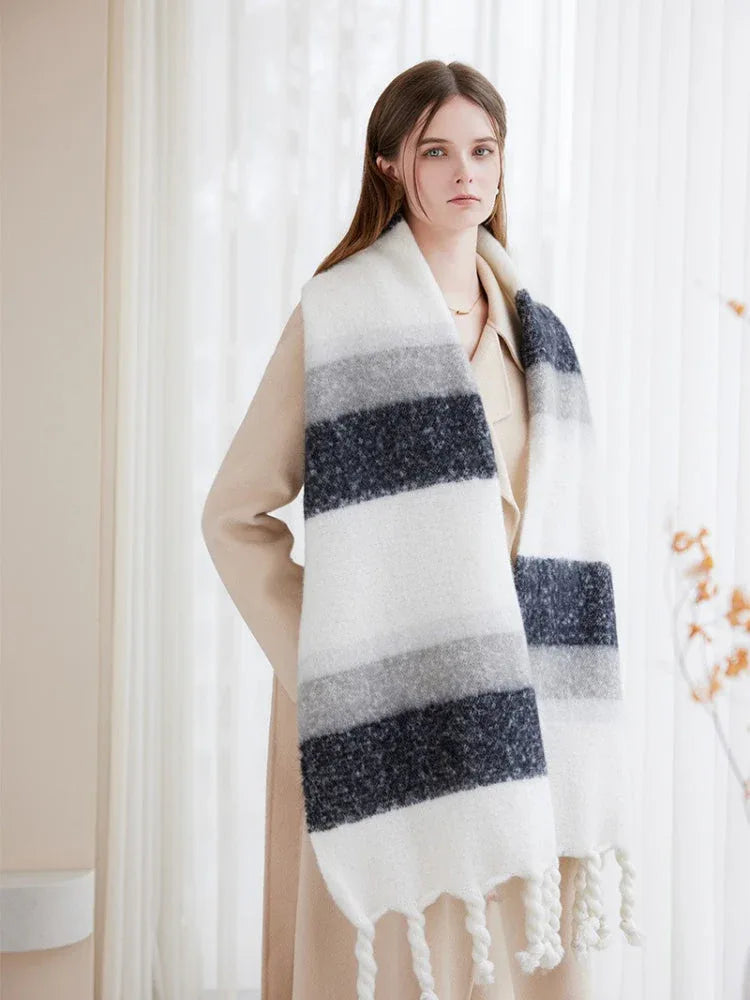 Close-up of a woman wearing a cream coat and a large, striped scarf with white, grey, and dark blue bands.