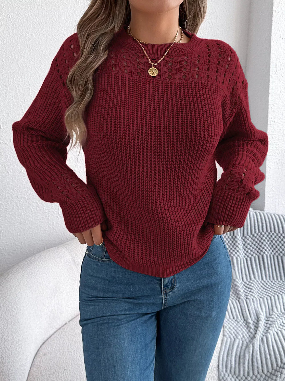 Woman wearing a maroon knit sweater with open-knit detailing and blue jeans