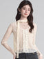 Woman wearing a cream-colored sheer lace long-sleeve top with ruffle detailing and a scarf detail.