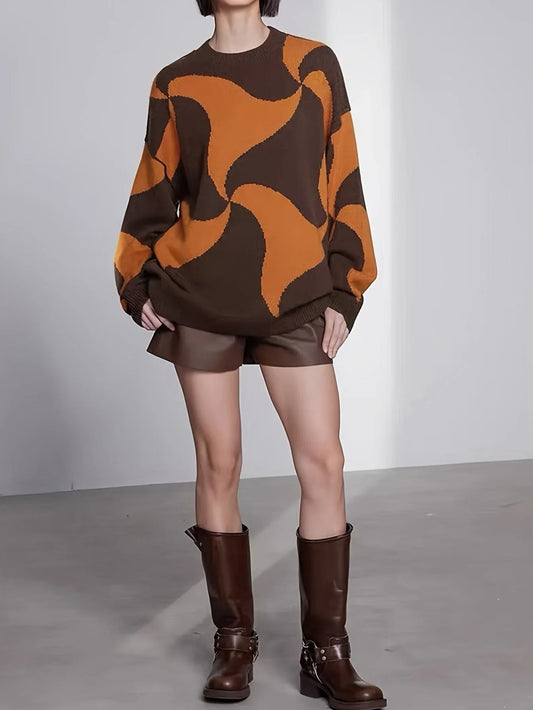 Woman wearing a brown and orange abstract patterned oversized sweater with brown leather shorts and brown boots.