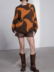 Woman wearing a brown and orange abstract patterned oversized sweater with brown leather shorts and brown boots.