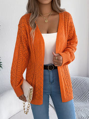 Close-up of a woman wearing an orange open-front knit cardigan, layered over a white tank top and blue jeans, accessorized with gold necklaces and rings.