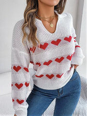Close-up of a woman wearing a white knit sweater with red heart pattern and blue jeans